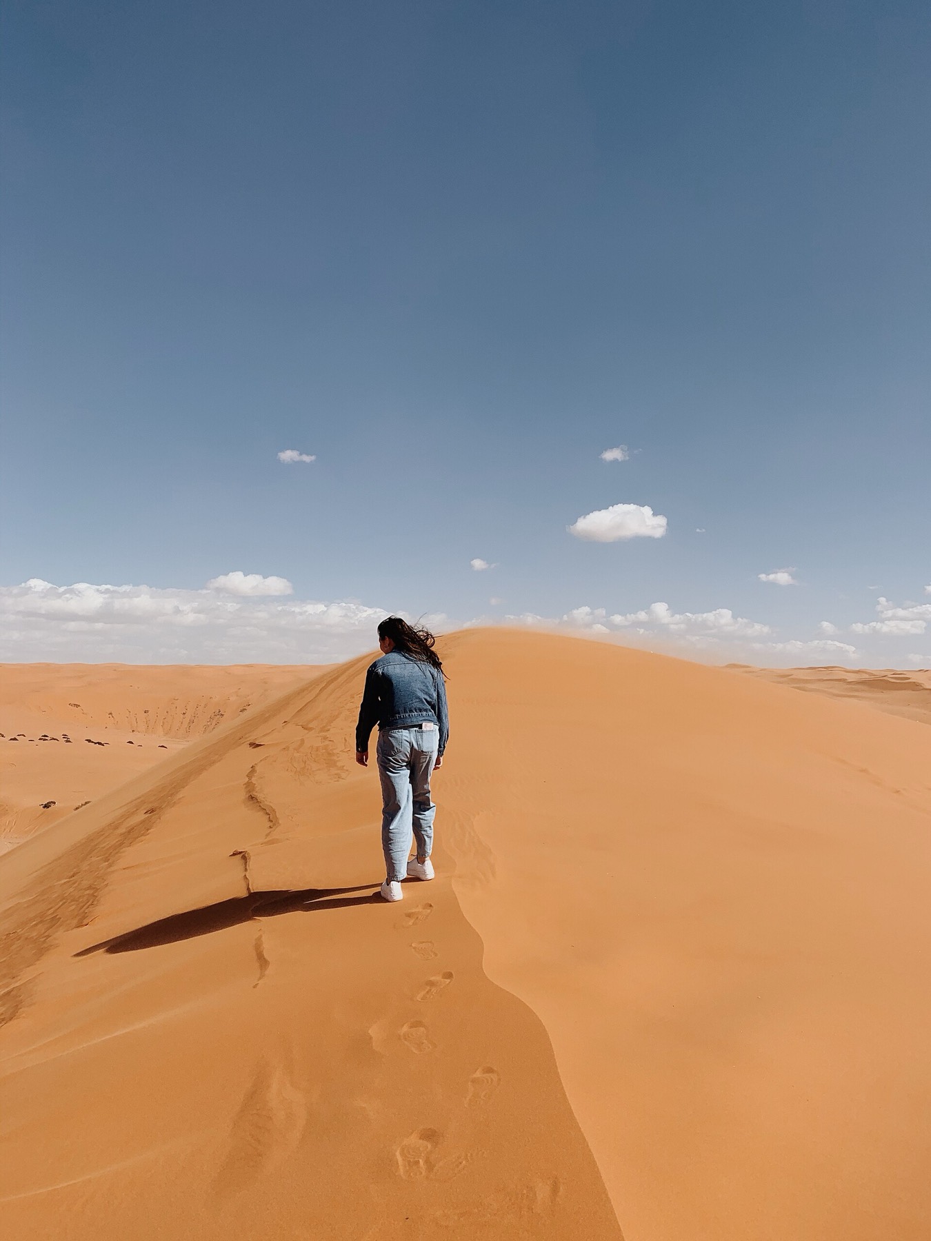 A person walking slowly along the crest of a sand dune in Saudi Arabia