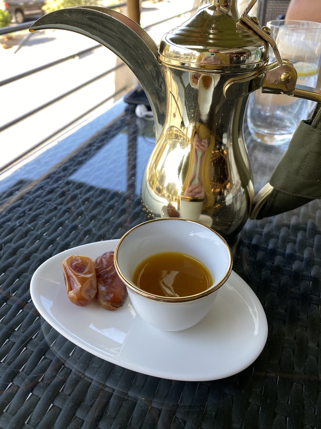 A cup of Arabic coffee with dates beside a silver dallah