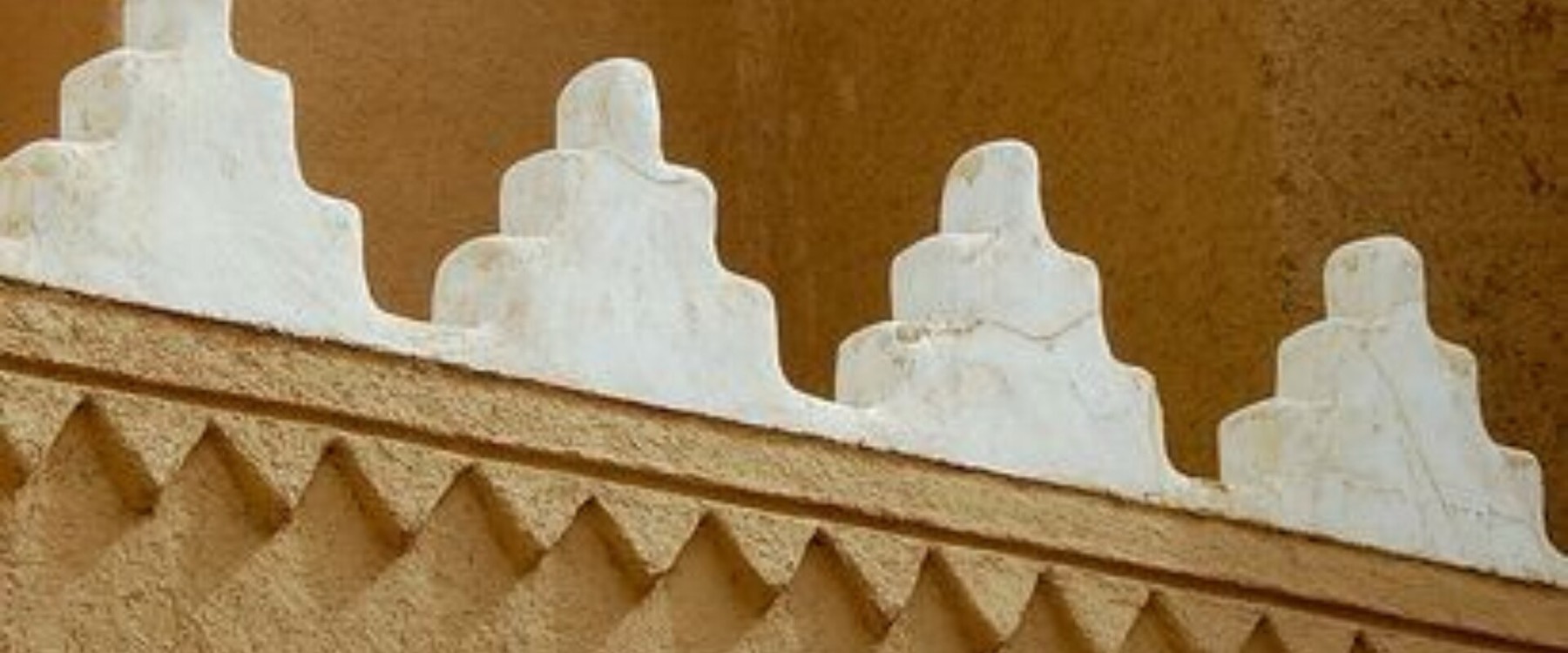Stepped white crenellations along a Najdi mud‑brick wall